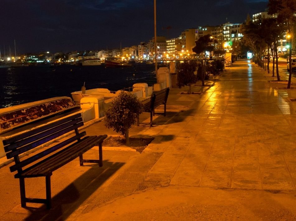 Malta travel guide - Quiet promenade along Gżira marina at night, with empty benches overlooking moored boats and city lights