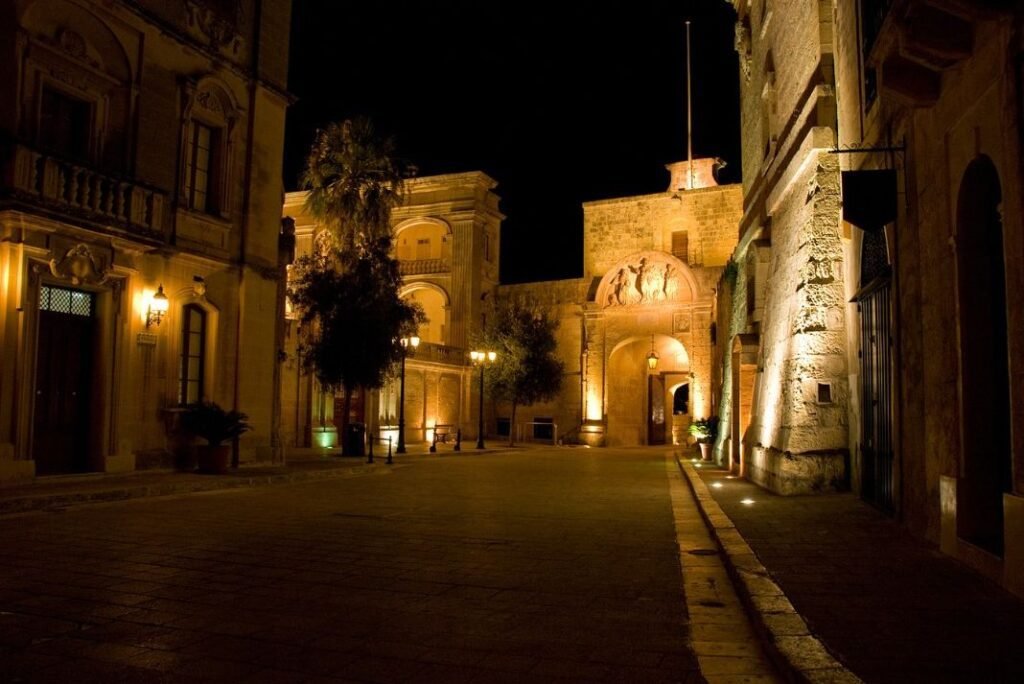 Malta travel guide. Main gate of Mdina, Malta, softly lit at night with golden tones and quiet empty streets