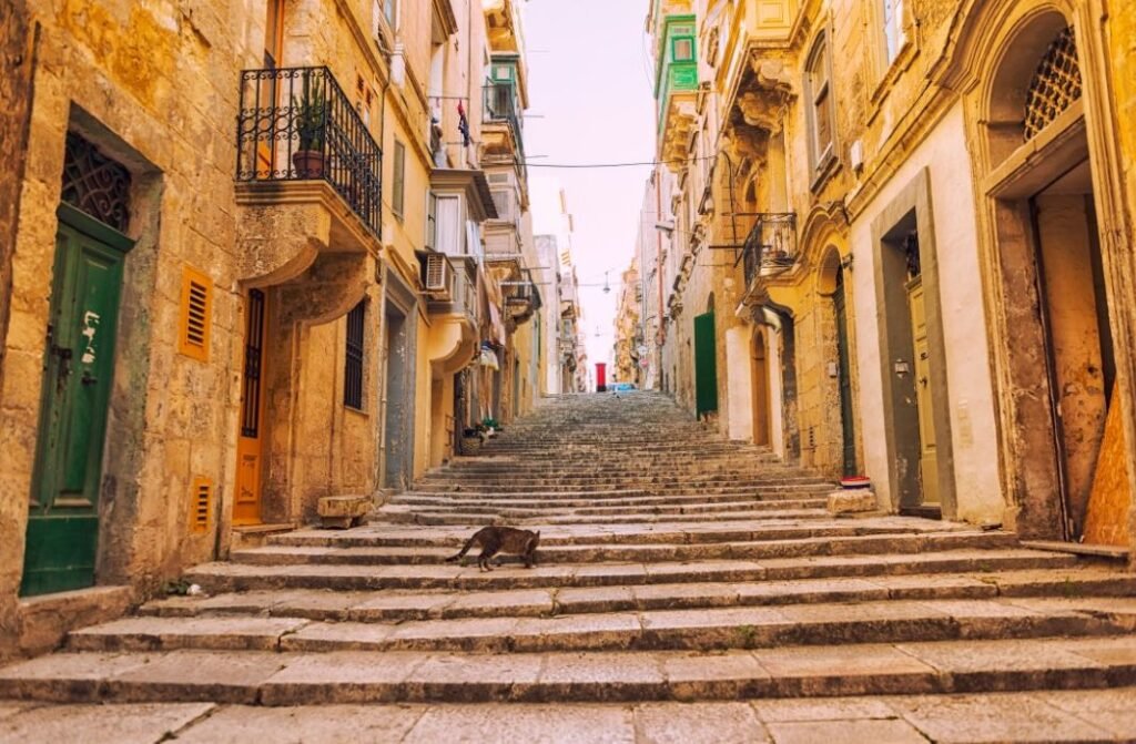 Steep stone staircase street lined with honey-coloured buildings in Valletta, Malta.