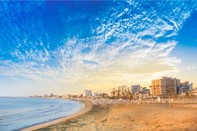 Cyprus travel guide  beachfront at sunset with golden sand, calm sea, and a dramatic sky filled with clouds.