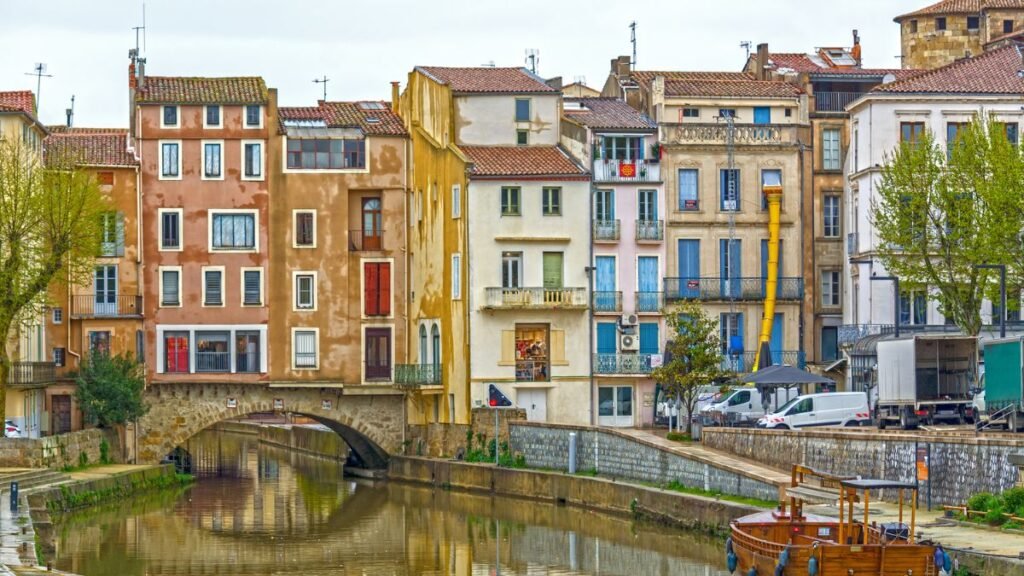 Traditional pastel-coloured buildings reflecting in the canal in Narbonne, Southern France