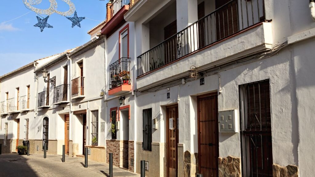 Row of traditional whitewashed townhouses with balconies and wooden doors on a quiet Spanish street.